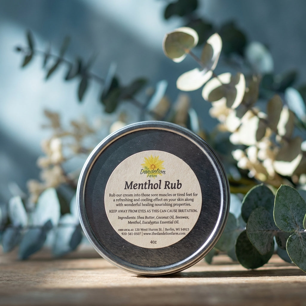 An artistic studio setup featuring the Menthol Rub jar prominently in the foreground, lit by a rim light to create a luminous outline that accentuates its round shape and textured label. The background consists of blurred botanical elements and eucalyptus