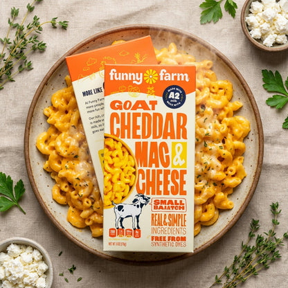 A vibrant, studio-style product shot from a bird’s-eye view with the Goat Cheddar Mac & Cheese served on a rustic, round ceramic plate. Bright, HDR studio lighting eliminates shadows and enhances the vivid, orange color of the cheese. Visible steam rises f