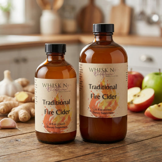 A high-resolution studio shot of a glass bottle labeled 'Traditional Fire Cider' placed on a rustic wooden table, illuminated with softbox lighting to highlight its amber color and textured label. The background features a softly blurred kitchen counter wi