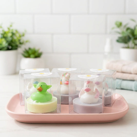 A vibrant product shot of Little Buds Soaps displayed on a soft pastel-colored ceramic tray in a bright, airy bathroom setting. The scene is illuminated with softbox lighting, highlighting the smooth, colorful soap and the adorable animal toy on top. The c