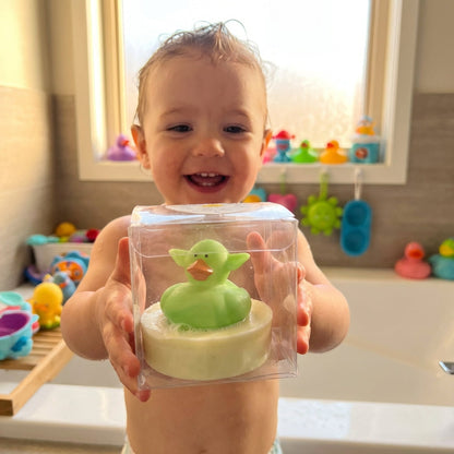 A lifestyle scene showing a happy child in a modern bathroom, holding a Little Buds Soap with the animal toy clearly visible. The camera is positioned at a child's eye level, using a wide-angle lens with a shallow depth of field to focus on the child's del