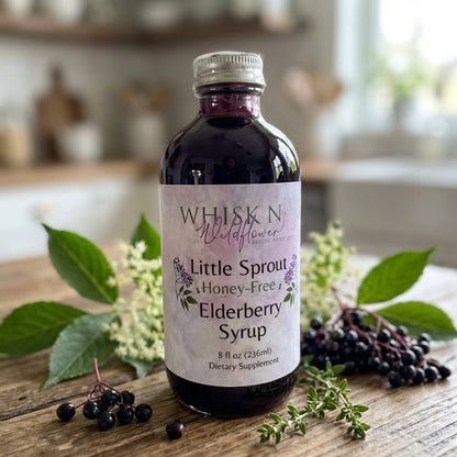 A close-up shot of the Little Sprout Elderberry Syrup bottle placed on a rustic wooden surface, illuminated by softbox lighting to highlight the rich, dark purple hue of the syrup inside a clear, BPA-free plastic bottle. The scene includes a backdrop of fr