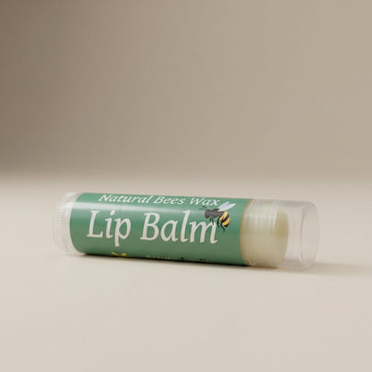 A close-up shot of the 'Natural Bees Wax Lip Balm' set against a soft, neutral beige background under diffused daylight studio lighting. The camera, positioned at a slight angle with a 50mm lens, captures the sleek, matte texture of the lip balm tubes with