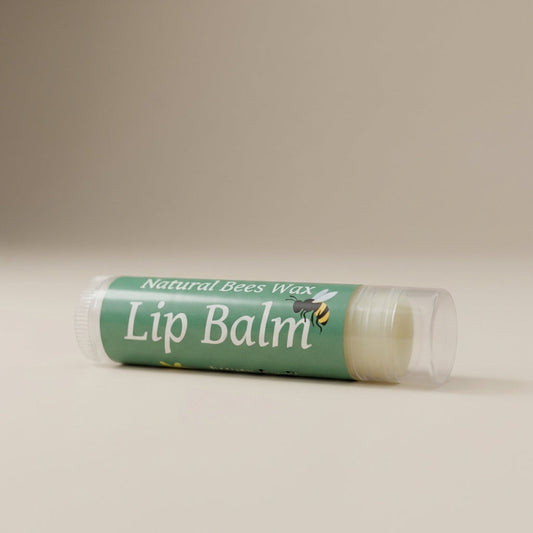 A close-up shot of the 'Natural Bees Wax Lip Balm' set against a soft, neutral beige background under diffused daylight studio lighting. The camera, positioned at a slight angle with a 50mm lens, captures the sleek, matte texture of the lip balm tubes with