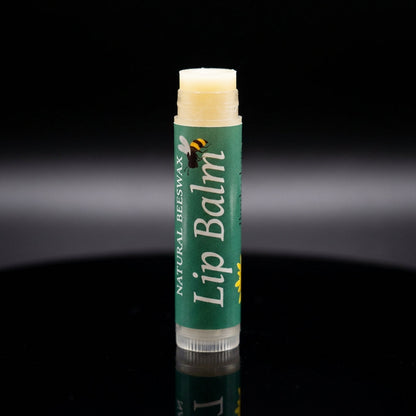 A studio product shot of the 'Natural Bees Wax Lip Balm' standing upright on a reflective black surface under sophisticated, softbox lighting. The camera, set with a macro lens at 100mm, captures minute details of the product’s embossed logo, the textured 
