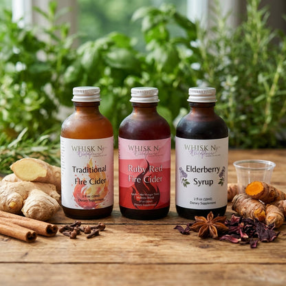 A vibrant, lifestyle-style setup featuring the 'Wellness Trio' displayed on a rustic wooden table beside fresh roots, spices, and hibiscus flowers, evoking a farm-to-table feel. The bottles are illuminated by diffused daylight, creating gentle shadows and 