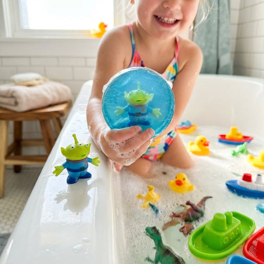Create a vibrant lifestyle scene showing a young child in a sunny, well-lit bathroom, about to enjoy a bath with the 'Soap Buddies.' Use natural diffused daylight to enhance the bright, inviting colors of the Soap Buddies, with soft rim lighting emphasizin