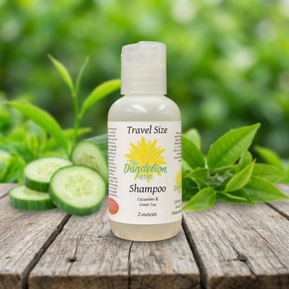 An outdoor lifestyle scene captured in natural daylight with a slight HDR effect, featuring the travel-size shampoo placed on a rustic wooden table outdoors. The scene highlights the soothing, textured label with vibrant green accents and imagery of cucumb