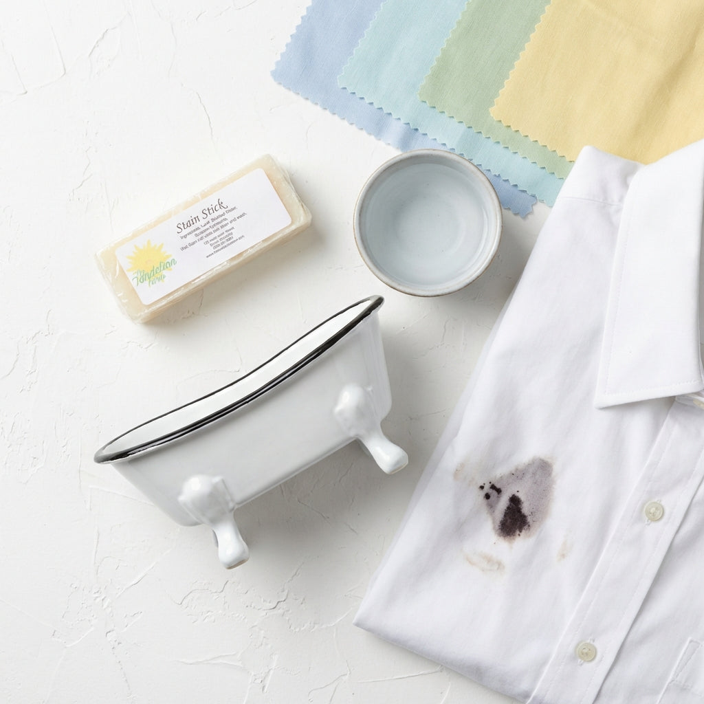 A stylish studio flat lay scene with the Stain Stick positioned diagonally across a clean, textured white surface. Professional diffused daylight studio lights create soft, even illumination, emphasizing the product's smooth, glossy plastic casing with sub