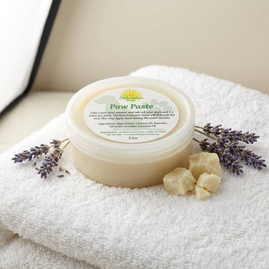 A high-resolution studio shot of 'Paw Paste' displayed in a matte, clear glass jar with a white, fluffy terrycloth towel beneath. The scene employs softbox lighting to highlight the creamy texture of the paste and the natural ingredients like Shea Butter a