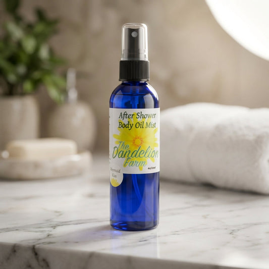 A high-resolution studio shot of the 'After Shower Body Oil Mist' placed on a sleek marble countertop, illuminated by a softbox light to highlight its transparent glass bottle and metallic spray cap. The background features a soft, blurred bathroom setting