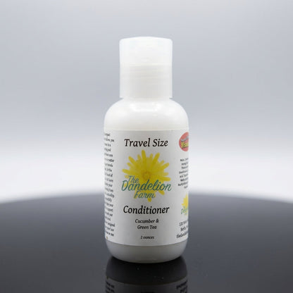 A sleek, close-up studio shot of the travel-size Hair Conditioner arranged on a reflective black surface, illuminated by softbox lighting that highlights the transparent green-tinted bottle and subtle text on the label. The background is a clean, gradient 