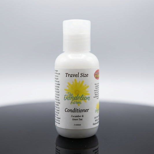 A sleek, close-up studio shot of the travel-size Hair Conditioner arranged on a reflective black surface, illuminated by softbox lighting that highlights the transparent green-tinted bottle and subtle text on the label. The background is a clean, gradient 