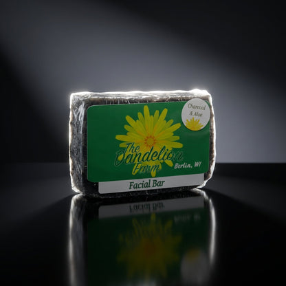 A clean, minimalist studio setup with a single facial bar placed on a reflective black surface, lit by a rim light that creates a striking halo effect around the soap. The focus is sharp, highlighting the soap’s textured surface and intricate natural ingre