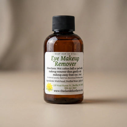 A close-up shot of an elegant, transparent glass bottle of Eye Makeup Remover, illuminated with softbox lighting that accentuates its sleek, minimalist design, set against a smooth, neutral-toned backdrop. The camera uses a macro lens at 100mm focal length