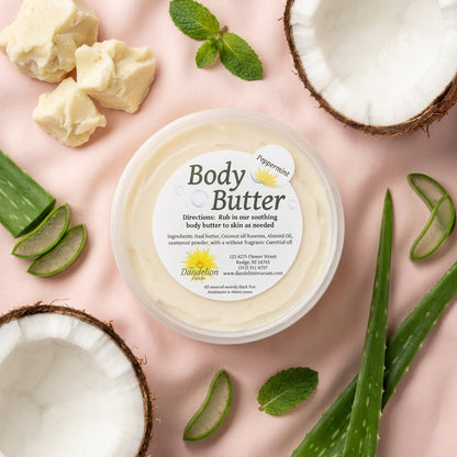 An elegant product flat lay arrangement displayed on a soft, pastel-colored fabric background. The jar of body butter is accompanied by natural ingredients like shea butter, coconut, and aloe vera leaves, artfully arranged to evoke freshness and natural go