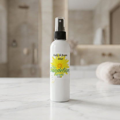 Capture a premium product shot of the 'Body & Room Mist' set against a sophisticated, softly blurred luxury bathroom background. Use a softbox lighting setup to create gentle, even illumination that highlights the reflective glass bottle with a sleek, mini