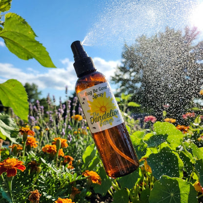A dynamic action shot depicting the 'Bug Be Gone Spray' being spritzed in a bright outdoor garden setting. The camera is positioned at a slight angle, using a 24mm wide-angle lens to include vibrant greenery, blooming flowers, and a clear blue sky in the b