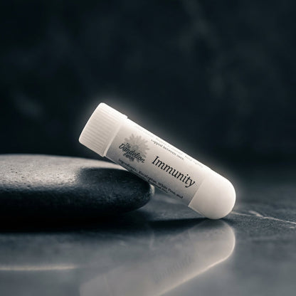 Create a dramatic, cinematic shot of the Aroma Sticks inhaler leaning against a smooth, dark stone surface, illuminated by a rim light that creates a halo effect around the product. Use a 85mm prime lens with a shallow depth of field to isolate the inhaler