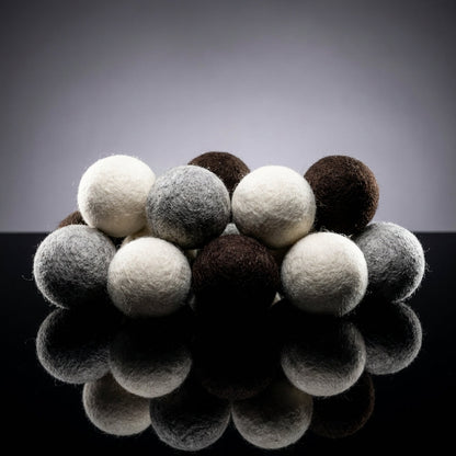 A high-contrast, studio-lit product display with multiple wool dryer balls arranged artistically on a reflective black surface, shot with a 50mm lens to create a slightly compressed perspective. Use rim lighting to accentuate the spherical shape and textur