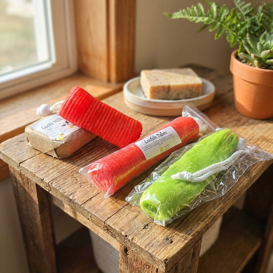 A vibrant lifestyle scene showcasing the Loofah Tubes arranged artfully on a rustic wooden bathroom shelf, with warm natural daylight streaming through a nearby window. The camera angle is slightly elevated with a 50mm lens, capturing the full length of th