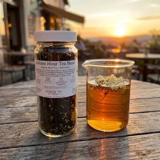 Golden Hour Tea Blend steeping in a beaker at an outdoor café table during sunset, with elderflower blossoms floating on top.