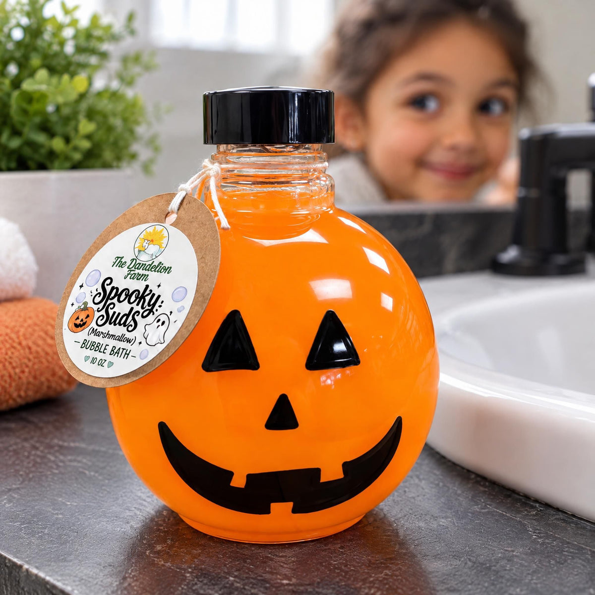 Orange pumpkin bubble bath bottle with marshmallow scent sitting near a white ceramic washbasin.