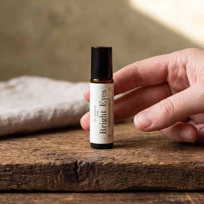Close-up of a small 'Bright Eyes' under eye serum bottle on textured dark wood with natural lighting.